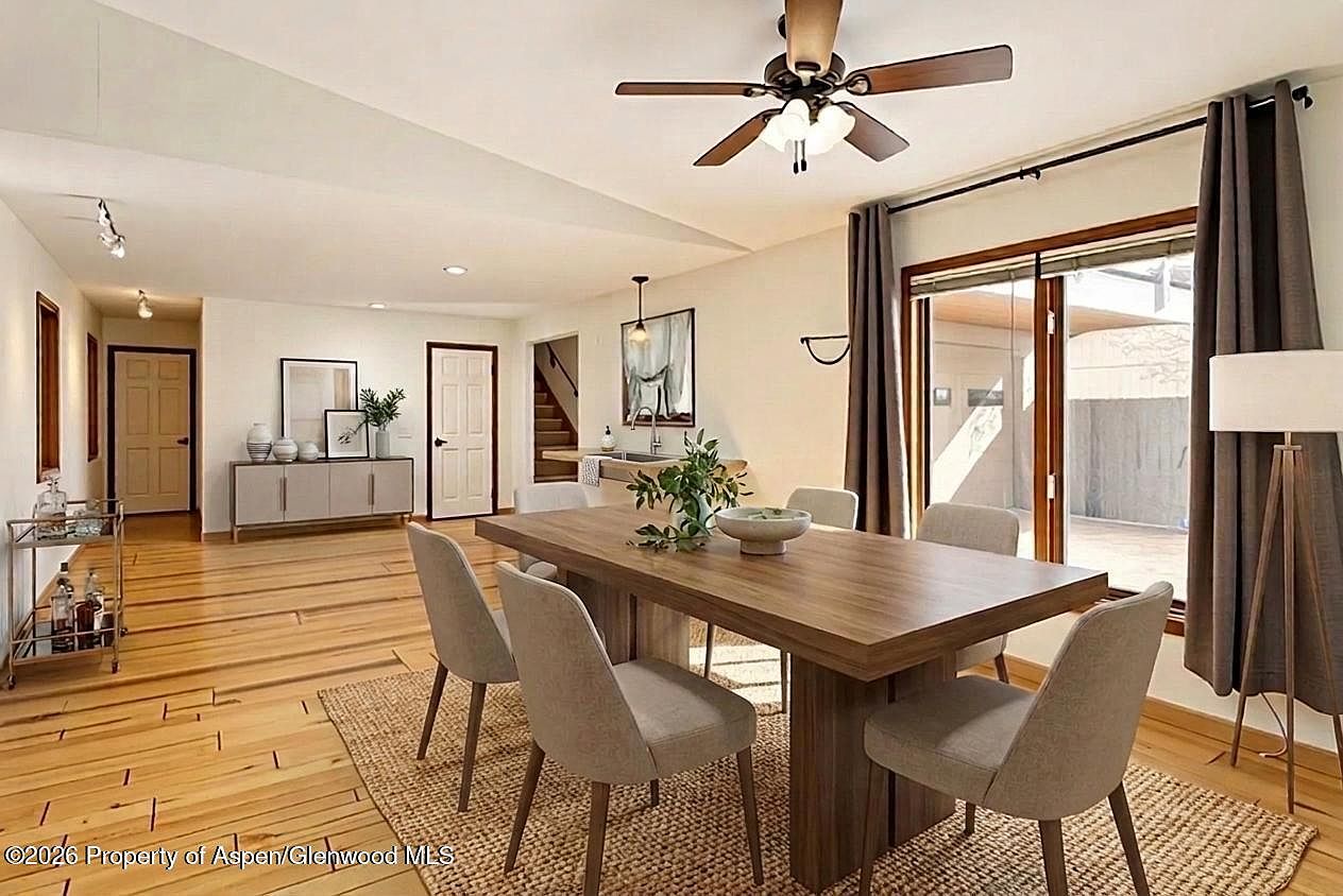 Dining room with long wood table, six upholstered chairs, sliding glass doors opening to the back deck, hardwood floors continuing throughout