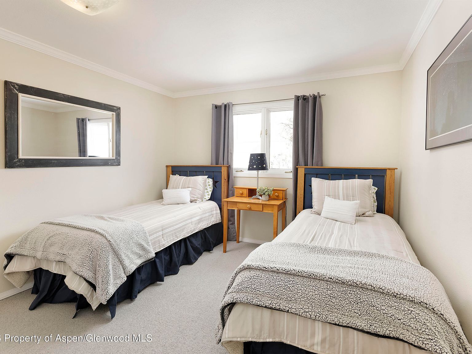 Secondary bedroom with twin beds, crown molding, twin framed windows draped in dark navy, neutral carpet and warm cream walls